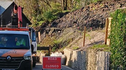 A road closed sign and a van parked on a hill next to a collapsed bank.