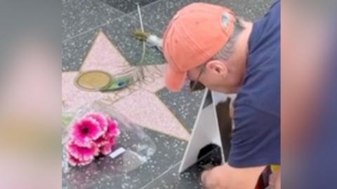 A man crouching down next to the Hollywood Walk of Fame star for Dolly Parton.