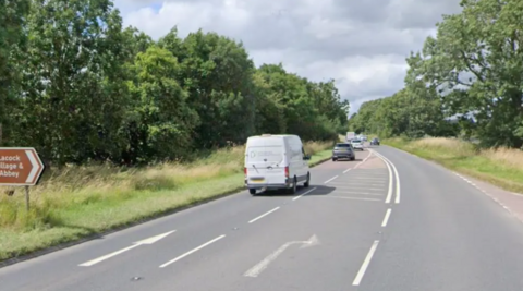 A single-lane road with grass on either side and road markings indicating a right-hand turn.