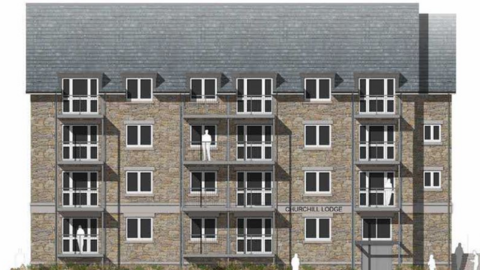 A large block of brick-built flats with balconies and windows and a pitched slate roof with a sign on the building saying Churchill Lodge.