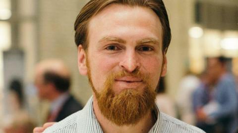 Karl Hinett, a man with swept-back reddish hair and a gingery beard, smiles at the camera.