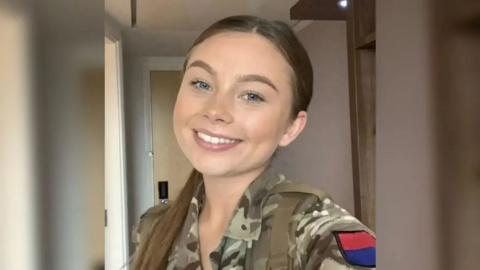 Jaysley Beck smiles in a selfie, taken inside a room, wearing her Army uniform
