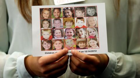 A woman holds up a memorial collage with pictures of the twenty child victims