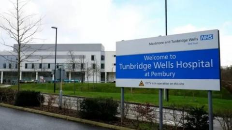 A hospital sign in blue with a hospital building in the background