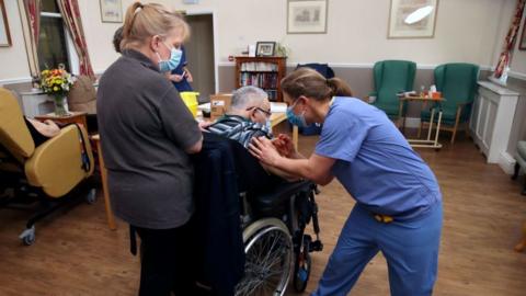 An elderley man in a wheelchair received a vaccination from a nurse in a care home