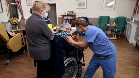 An elderley man in a wheelchair received a vaccination from a nurse in a care home