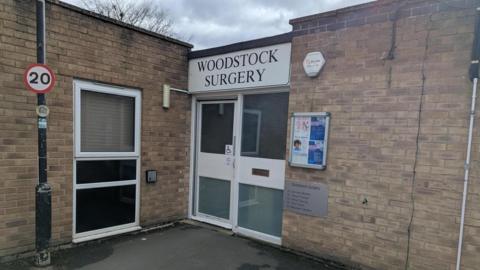 The front of Woodstock Surgery - which is a small flat roofed building on the bend of a road.