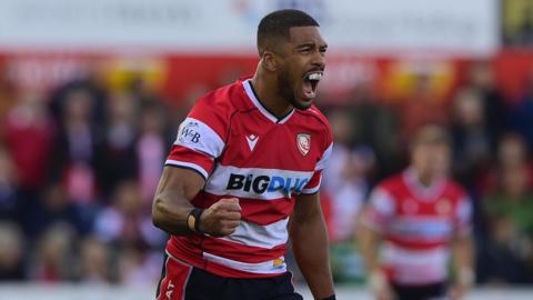 Ben Loader clenches his right fist and has his mouth open while standing on the pitch during a match for Gloucester