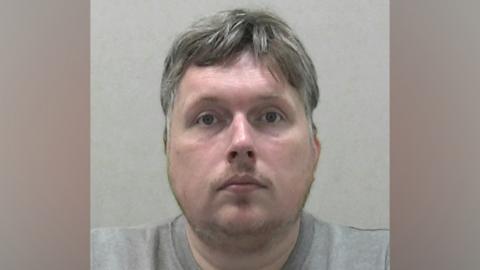 A mugshot of Ross Clancy. He has a patchy goatee and he grey hair.