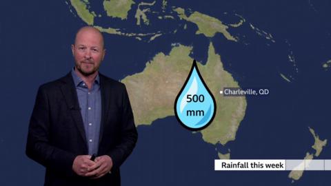 Darren Bett stands beside a rainfall graphic for Queensland, Australia