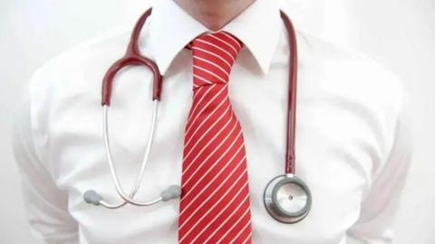 A close up of a man wearing a white shirt and red stripy tie, with a stethoscope around his neck.