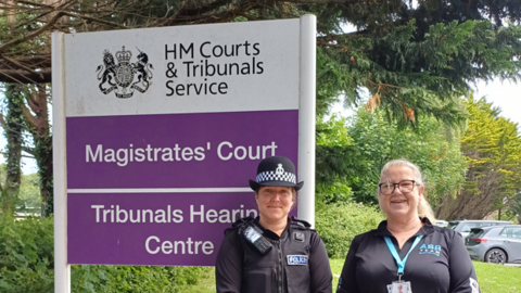Sgt Alice McKinnon (left) and Kay Smith, anti-social behaviour officer for Camborne at Cornwall Council, stand next to a purple and white sign for Truro Magistrates' Court.