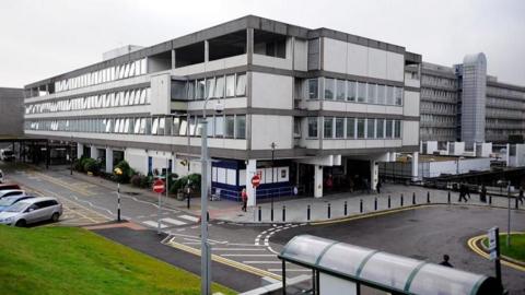 Aberdeen Royal Infirmary exterior shot of building on grey day with bus stop and cars parked in foreground