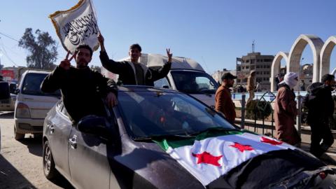 Syrian men celebrate from a car covered with a Syrian flag following a ceasefire agreement between the Syrian government and the Syrian Democratic Forces (SDF), in Raqqa, northern Syria (19 January 2026)