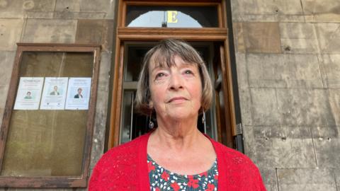 Councillor Val Walker wearing a red cardigan and standing in front of Edinburgh's City Chambers.