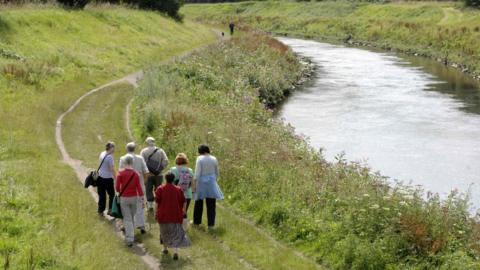 Picture of the Mersey River - walkers walk along the side of the river.