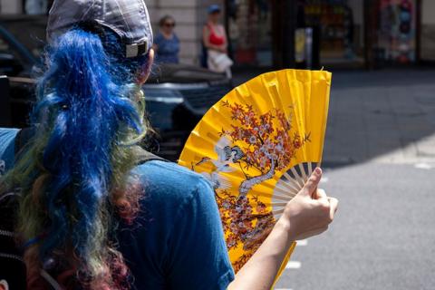 A woman cools herself with a yellow fan during a spell of hot weather