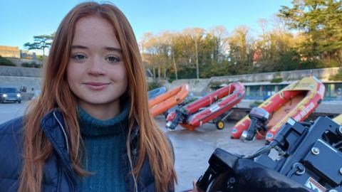 Student, Efa, is pictured alongside rigid-hull inflatable boats used in search and rescue operations 