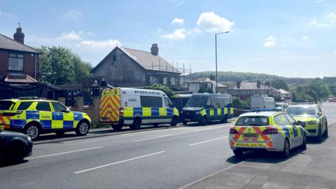 Police cars outside a house. The house has scaffolding, with the weather bright and clear.