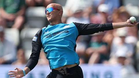 Fateh Singh is about to complete his bowling action in a white-ball game for Worcestershire. He is wearing black trousers and a top with black sleeves and light blue front. He is also wearing sunglasses
