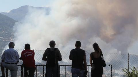 People look at smoke from a fire billowing over Carros, southeastern France,