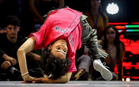 Morocco's Fatima Zahra El Mamouny, aka B-Girl El Mamouny, wears a baggy pink top as she arches her back to lean over upside down in a breaking move