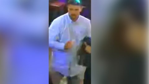 CCTV image showing a man with dark hair and short facial hair wearing a blue shirt and jeans.