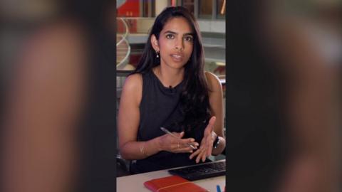 BBC Verify correspondent Merlyn Thomas with long dark hair at an office desk