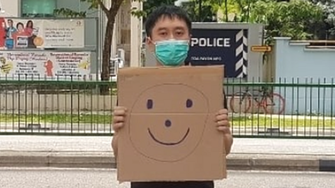 Jolovan Wham holds up a smiley face sign outside a police station