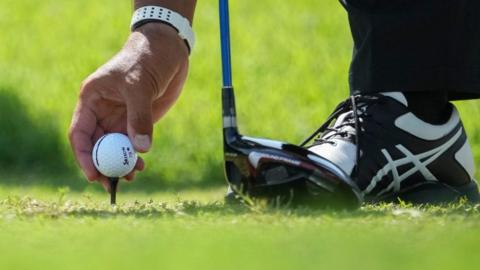Golfer placing ball on tee peg