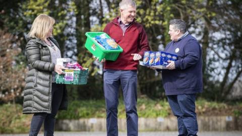 Scottish Liberal Democrat Leader Willie Rennie holds basket of food while speaking to two people