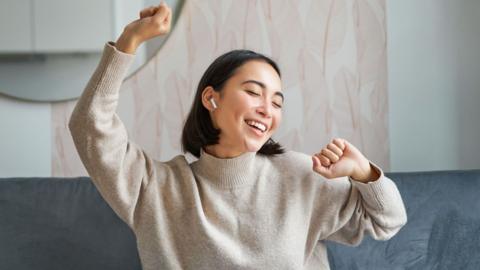 A woman sitting on the sofa and dancing to music.