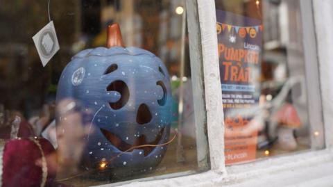 A blue pumpkin in a shop window with a 'pumpkin trail' sign next to it and fairy lights.