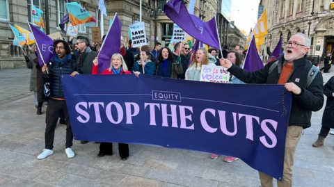 Men and women with banners and flags angry at council cuts gather outside the council's offices