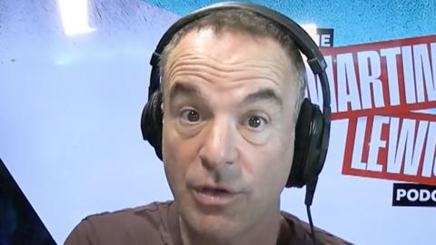 Martin Lewis wearing headphones and talking to the camera in front of a 'The Martin Lewis Podcast' sign