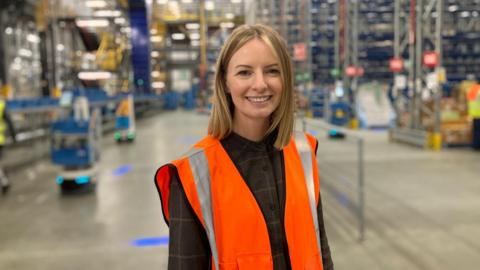 Jenna Whittingham-Ward wearing an orange hi-vis jacket stood in a warehouse