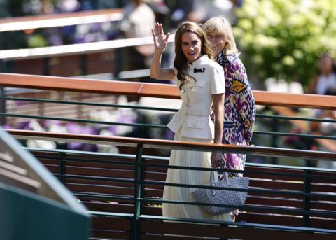 The Princess of Wales waves to people at Wimbledon. She is wearing a cream, pleated skirt and cream, belted blazer. She has long brown hair.