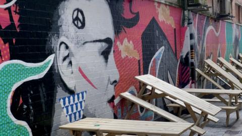 A wall with artwork dedicated to the punk movement with wooden benches leaning against the wall