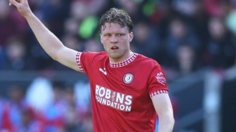 Bristol City defender Rob Dickie, with his right arm aloft. He has short dark hair and is wearing the red home kit of Bristol City.