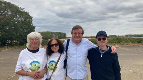 A group of four people standing next to each other. The two women are wearing white T-shirts with the campaign group logo. Two people are wearing sunglasses and two are wearing glasses.
