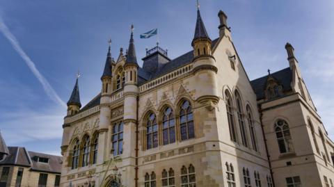 Built to a Flemish-Baronial style, Inverness Town House is a sandstone building with turrets and ornately designed windows. A Saltire flag flutters from a pole on the roof.