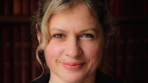 Headshot of Hilary Pullum, who has dark blonde hair that has been tied up and hazel-coloured eyes.  