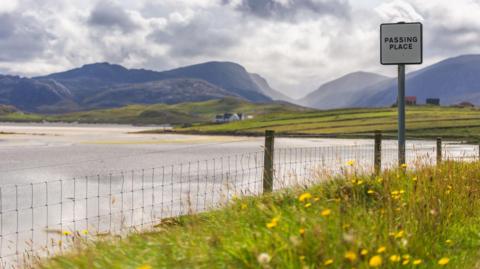 Beanntan ann an Ùig ann an Leòdhas le sgothan os an cionn, taigh ri taobh na traghad, loch àir cùlaibh feansa agus soidhne air rathad singilte.