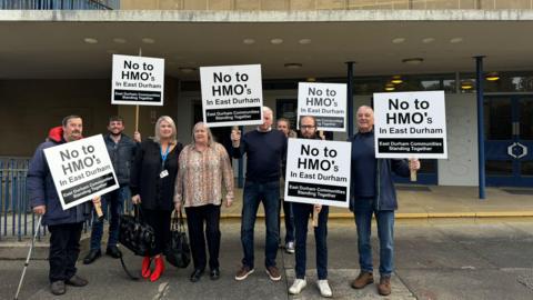 Eight members of East Durham Communities Standing Together group standing outside Durham County Hall and holding signs which read  No to HMO's in East Durham.