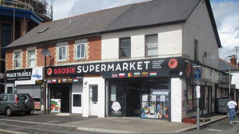 The front of Grosik Supermarket after the extension has bee removed. A person is seen walking down one of the side streets.