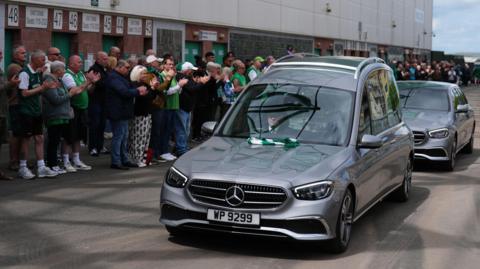 A silver hearse with the coffin of Sir Tom Farmer drives past supporters gathered outside Easter Road Stadium in Edinburgh