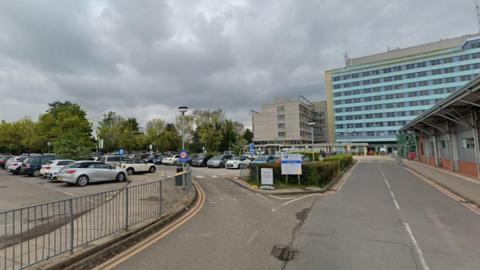 A Google Maps view of the exterior of Boston Hospital. There are two roads – one leading to the building and one leading to a car park on the left. The sky is overcast.