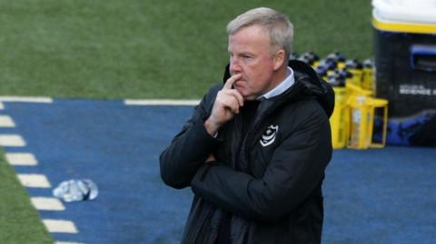 An image of Kenny Jackett, wearing a black jacket with the Portsmouth crest on the front, looking pensive on the touchline at Fratton Park during Pompey's game against Wigan in September 2020