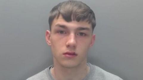A mugshot of Jack Lawson, who is looking blankly into the camera. He has short brown hair and is wearing a grey jumper.