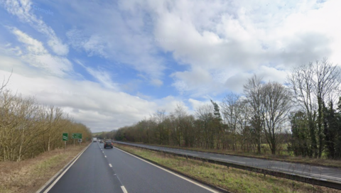 A view of the A303 near Wylye in Wiltshire. Cars are driving away from the camera in the distance. It is cloudy.